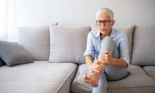 Middle-aged woman suffering from pain in leg at home, closeup. Physical injury concept. Ankle pain, painful point. Problems with feet, joints, legs and ankles.