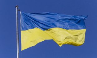 close up of waved Ukrainian flag on flagpole against blue sky